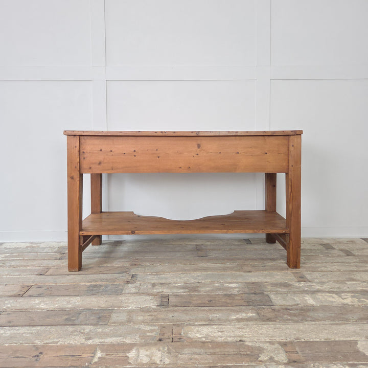 A Victorian pine farmhouse table from the 19th century with planked top, two drawers and lower shelf, raised on chunky legs. Originally used as a prep table, it is equally suited to life as a serving table, console or sideboard. This antique pine work table combines straightforward design with useful storage, making it a versatile Victorian piece for the kitchen, dining room or hallway in any farmhouse or rustic interior.