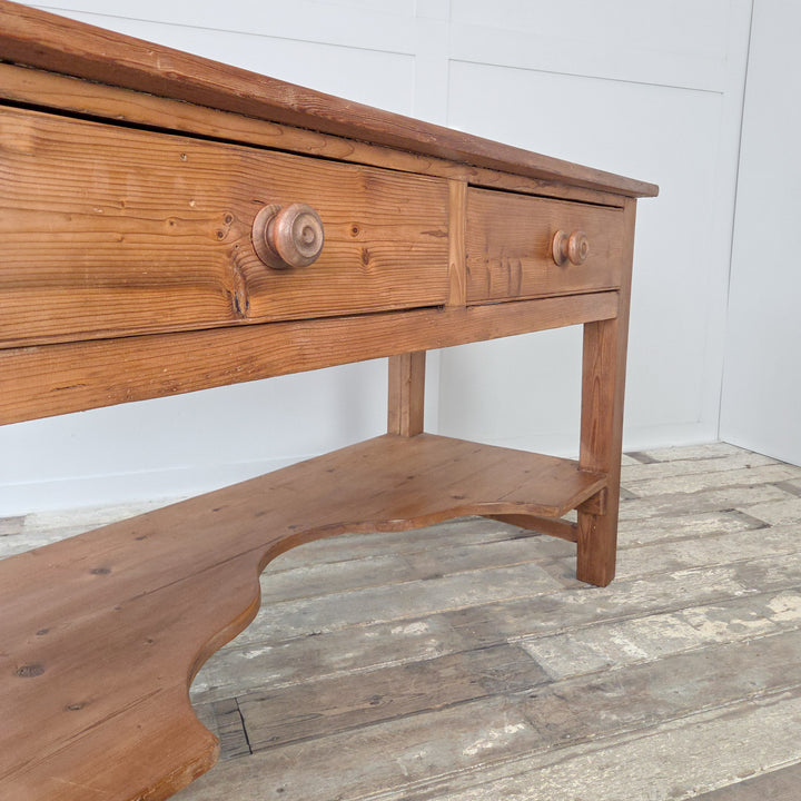An antique Victorian pine kitchen prep table from the 19th century, built in solid pine with a substantial planked top, two drawers and a shaped lower shelf. This versatile farmhouse table with chunky straight legs can be used as a rustic serving table, a console in the hallway, or as a farmhouse sideboard. A classic example of Victorian pine furniture offering both storage and surface space in one functional form.