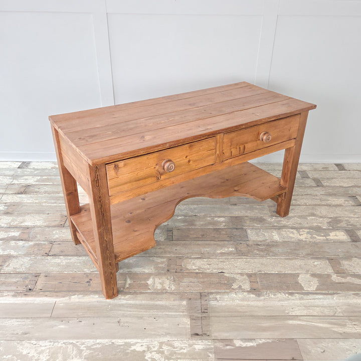 An antique Victorian farmhouse prep table from the 19th century in solid pine, fitted with two drawers and a shaped lower shelf below a broad planked top. Raised on sturdy straight legs, this versatile piece can serve as a rustic kitchen prep table, a functional work table, or be placed in a hallway as a console or in a dining space as a serving sideboard. A practical and authentic example of Victorian pine furniture designed for everyday use.