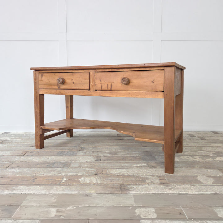 A 19th century Victorian pine console table with planked surface, twin drawers and lower shelf, built for use in farmhouse kitchens. This antique pine table can be styled as a rustic serving table, a sideboard in the dining room, or as a console in a hallway. Sturdy and practical, it reflects the straightforward design of Victorian furniture while offering storage and display space for modern interiors.