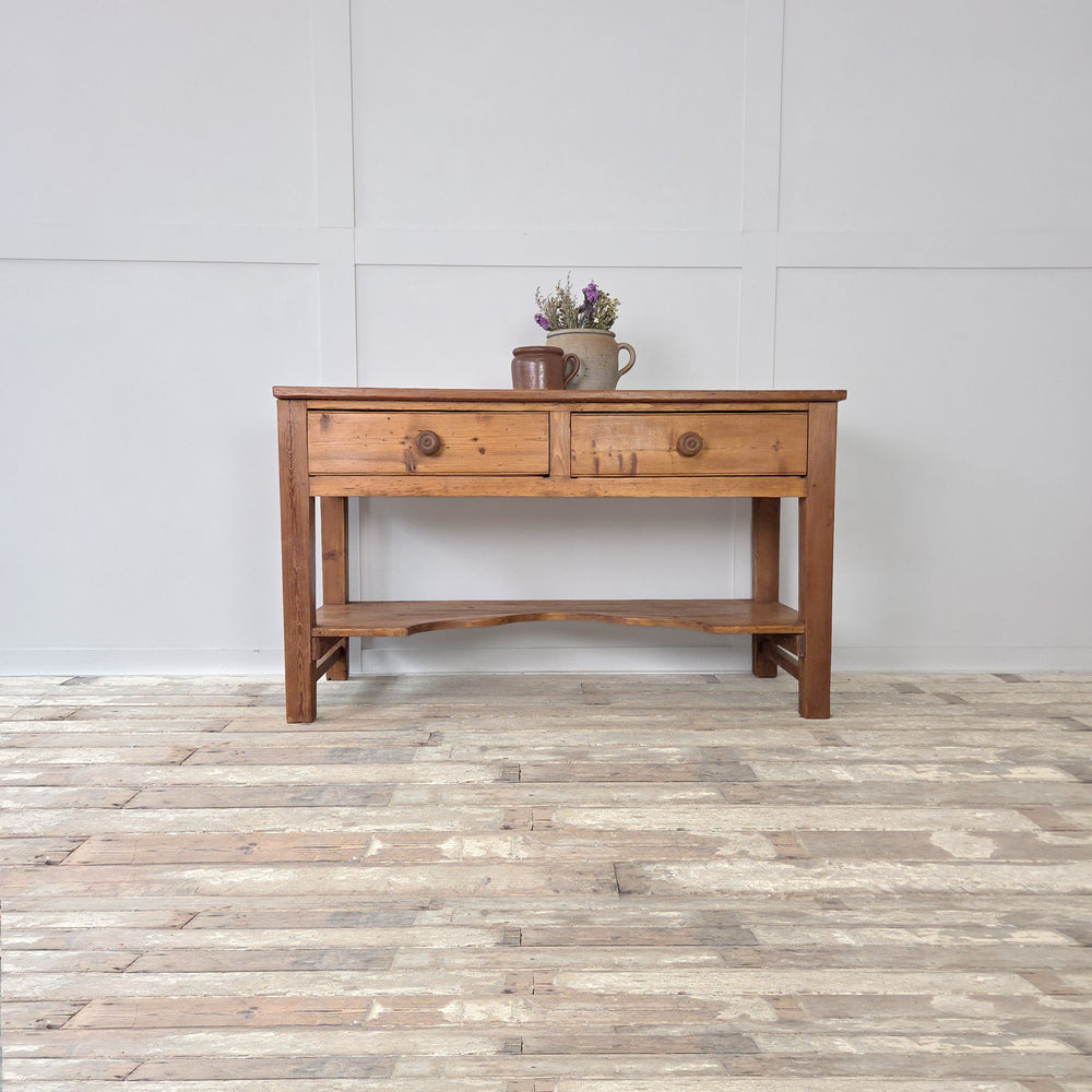 An antique 19th century Victorian pine prep table with farmhouse character, featuring a substantial planked surface, two practical drawers and a shaped lower shelf. Supported on chunky straight legs, this authentic piece of pine furniture works equally well as a rustic kitchen prep table, a serving or sideboard table in a dining space, or as a console table in a hallway, blending storage and display in one useful form.