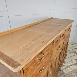 A 19th-century country pine dresser base with seven drawers in mixed sizes, three cupboards and matching brass fittings. The lighter scrubbed top with cleated ends contrasts with the original base, forming a practical farmhouse style sideboard.