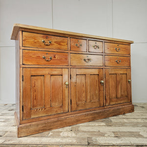 A 19th-century pine kitchen dresser offering seven drawers, three cupboards and brass handles. The scrubbed pine top, added later, provides a lighter surface that complements the rustic pine base, creating useful storage for everyday items.