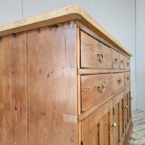 A rustic pine dresser base from the 19th century with seven drawers, three cupboards and matching brass swan-neck handles. The lighter scrubbed top with cleated ends adds contrast, forming a substantial country house style sideboard.