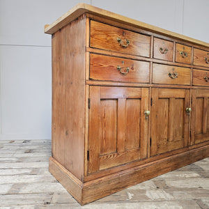 A 19th-century farmhouse style kitchen dresser with a deep-toned pine base, lighter scrubbed top and cleated ends. Seven drawers and three cupboards fitted with brass handles make this a functional sideboard for home storage.