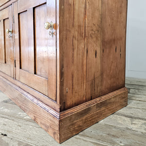 A country house style 19th-century pine dresser base with seven drawers, three cupboards and uniform brass fittings. The later scrubbed pine top in a lighter tone offers a clean contrast, creating a practical rustic pine storage piece.