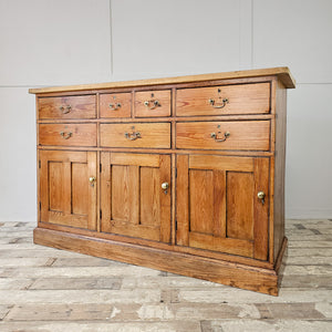 A substantial 19th-century country pine dresser base fitted with seven drawers, three cupboards and matching brass hardware. The scrubbed pine top with cleated ends gives a lighter appearance above the rich rustic base.