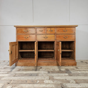 A farmhouse style 19th-century dresser base with a scrubbed pine top, seven assorted drawers and three cupboards. Brass swan-neck handles add simple detailing, making this rustic pine sideboard a functional storage piece.