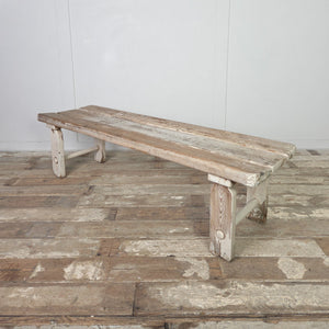 A country pine bench from the early 20th century, constructed with a three-plank top and straight legs connected by circular lower stretchers. Suitable for use in a hallway, at the foot of a bed, or as a simple dining bench in a kitchen.