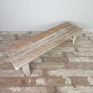 An antique farmhouse pine bench from the early 20th century, made with a three-plank top and straight legs with circular lower stretchers. This practical bench can be used in a boot room, hallway, or as a dining bench.