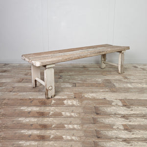 An antique early 20th-century rustic pine bench with a three-plank seat and straight legs joined by circular lower stretchers. This country bench lends itself to hallway use, bedroom placement, or use as a dining bench in a kitchen.