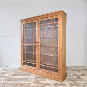 An early 20th century antique pine cupboard with glazed doors and frosted glass panels, offering spacious internal storage across adjustable shelves. This large cupboard is finished with a waxed finish and has the sort of straightforward country charm found in good pine furniture.