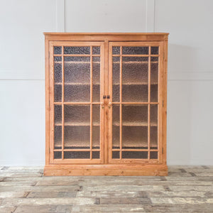 A beautiful farmhouse style pine cupboard from the early 20th century, featuring glazed double doors opening to reveal adjustable internal shelving. Sealed in a furniture wax to protect the pine, this rustic cupboard is a flexible storage piece with plenty of character.