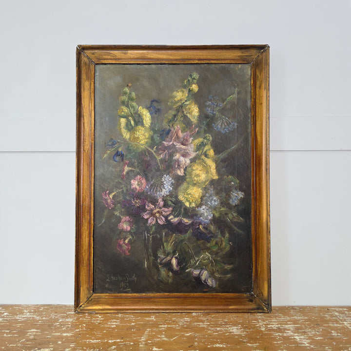 1929 signed oil painting by L Graham Smith featuring an arrangement of garden flowers rendered in oil on canvas. This antique artwork is complemented by a plain painted gilt frame.
