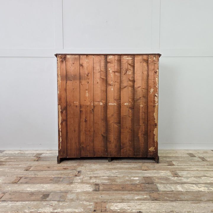 An early 20th-century pine chest in a deep dark stain, fitted with four drawers and brass cup handles. The chest has tongue-and-groove panelled sides and stands on a plinth base, its surface showing the natural patina and texture of well-aged pine