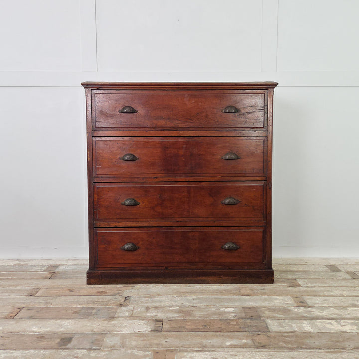 A substantial antique pine chest dating from the early 20th century, featuring four well-proportioned drawers fitted with brass cup handles. Made from solid pine with a dark stained finish and panelled sides, raised on a plinth base with visible wear that reflects its age.