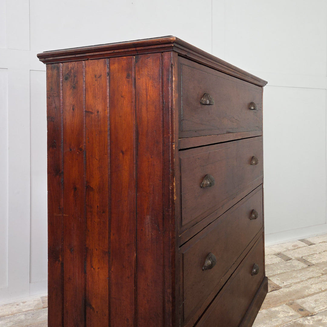An early 20th-century pine chest of drawers offering four deep drawers with brass cup handles. The dark stained pine shows the natural grain and tone of the wood, complemented by tongue-and-groove panelled sides and a plain plinth base typical of country pine furniture.