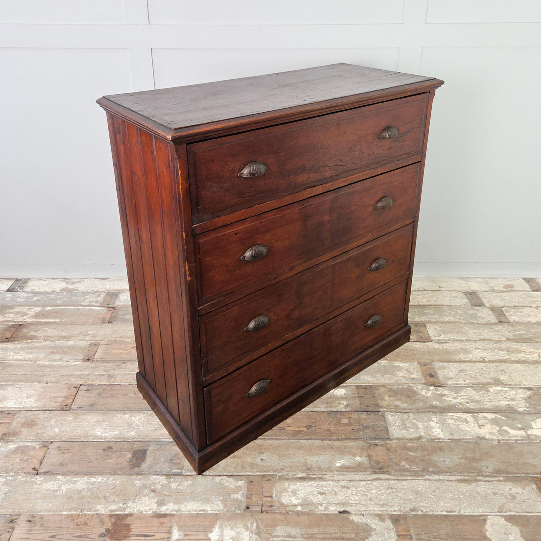 A well-made antique pine chest of drawers dating to the early 20th century, with four full-width drawers, brass cup handles, and a rich dark stained finish. The sides are tongue-and-groove panelled, and the chest stands firmly on a plinth base.