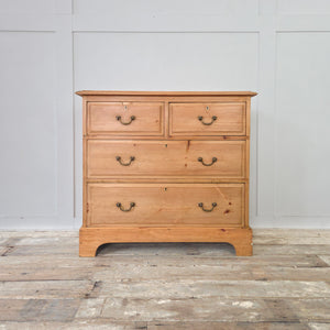 Antique pine chest of drawers dating from the early 20th century. Arranged with two short drawers over two longer drawers, all with original brass swan neck handles and escutcheons. The piece has a warm pine patina, a plinth base with decorative cut-out, and moulded top edges, offering functional bedroom storage.