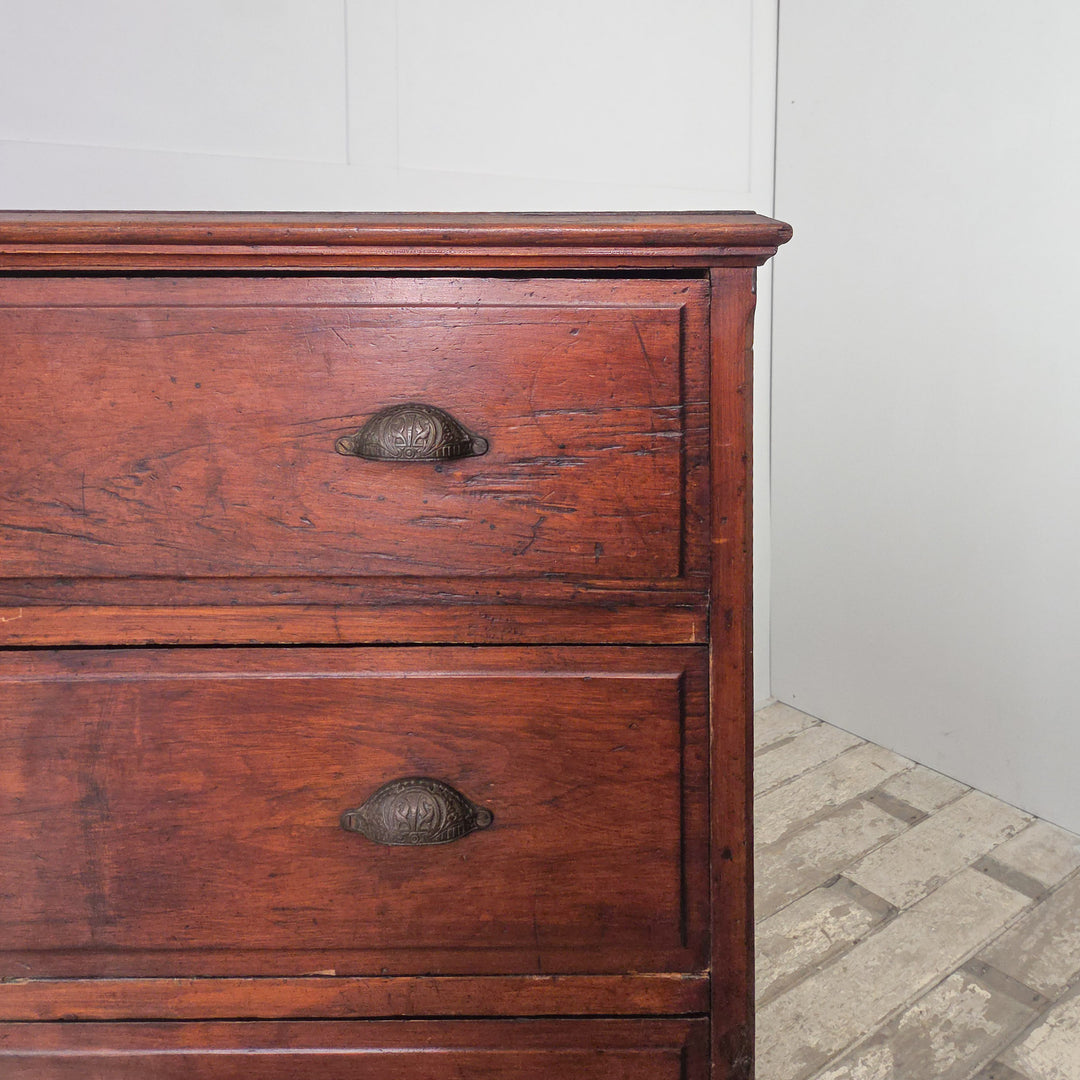 An early 20th-century pine chest featuring four drawers with brass cup handles and a dark stained surface. The simple moulded top, panelled sides, and plinth base highlight the sturdy proportions and practical design of traditional country furniture.