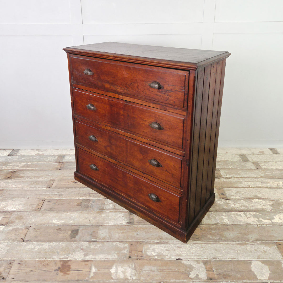 A dark stained antique pine chest of drawers from the early 1900s, offering four spacious drawers with brass cup handles. Constructed with panelled sides and a plain plinth base, showing the depth of colour and wear that develop with age and use.