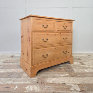 A vintage early 20th century pine chest of drawers in antique finish. This piece has four drawers in a two over two arrangement, original brass handles and escutcheons, and a natural pine patina. Sitting on a plinth base with decorative cut-out and moulded edges, it is sealed in clear wax for protection.