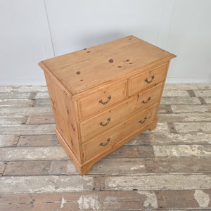 Early 20th century antique pine chest of drawers with four drawers, arranged as two short drawers over two long drawers. Retains original brass swan neck handles and escutcheons. Finished with a natural pine patina, plinth base, and moulded edges to the top, making a practical and attractive bedroom storage option.
