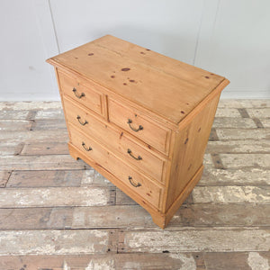 Antique pine chest of drawers from the early 20th century. Featuring four drawers in a two over two arrangement, original brass swan neck handles, and escutcheons. The chest has a natural pine patina, sits on a plinth base with decorative cut-out, and has moulded edges to the top. Finished with a clear wax seal.