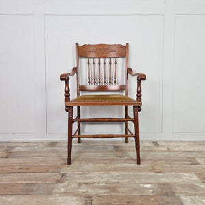 Antique Edwardian oak spindleback chair from the early 20th century, with floral carved detail to the crest rail, shaped armrests and a studded mustard velvet seat.