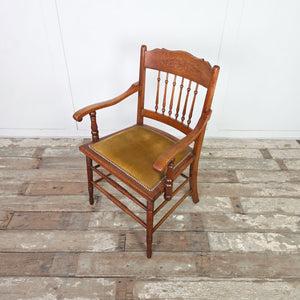 Antique oak spindleback chair with Edwardian floral carved crest rail, shaped armrests and ring-turned front legs beneath a velvet seat.