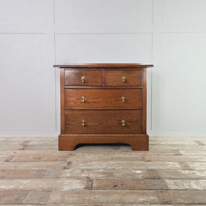 Antique Edwardian oak chest of drawers featuring four drawers arranged two over two, fitted with brass pear-drop handles, a moulded top with raised upstand and a shaped plinth base.
