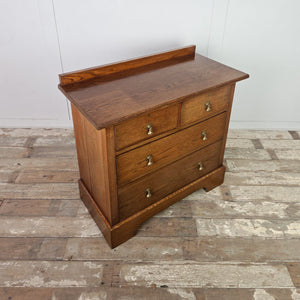 Edwardian oak chest of drawers from the early 20th century featuring four drawers, decorative brass drop handles, moulded edges to the top and a shaped plinth base.

