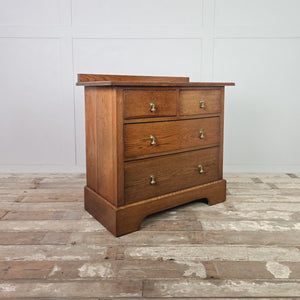 Edwardian oak chest of drawers from the early 20th century featuring four drawers, decorative brass drop handles, moulded edges to the top and a shaped plinth base.
