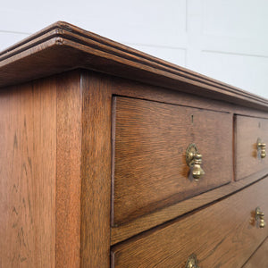 Antique Edwardian oak chest of drawers with a classic two over two drawer layout, brass drop handles, a moulded top with raised upstand and a shaped plinth base.
