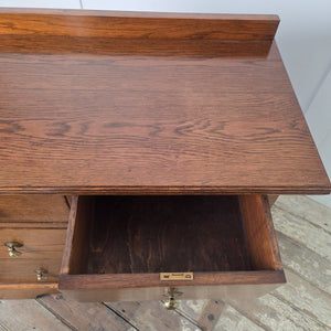 Edwardian antique oak chest of drawers featuring four drawers arranged two short over two long, with decorative brass drop handles and a shaped plinth base.
