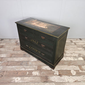 An early 20th century antique painted storage chest with four drawers and brass handles. The piece features a dark green painted surface with hand-painted lettering and lined detailing, along with a decorative ship scene painted to the top. Constructed in mahogany veneer and well suited to hallway or living room storage.