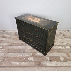 An early 20th century four drawer painted chest of drawers with a dark green painted finish and decorative hand-painted details. The top features a painted sailing ship scene, while the drawers have lined detailing and brass handles. Raised on a plinth base and suitable for use as a sideboard in a living space.
