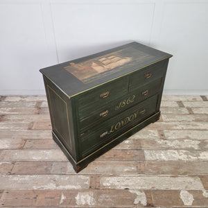 A painted antique chest of drawers dating to the early 20th century, featuring four drawers with brass handles and decorative hand-painted detailing. The dark green finish includes lined borders and lettering, with a painted ship motif to the top. Raised on a plinth base and useful as bedroom drawers.