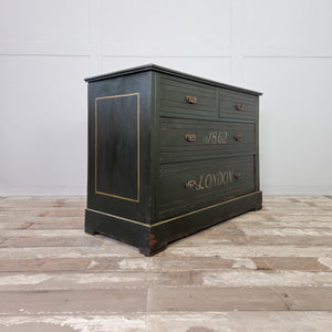 A four drawer antique painted chest dating from the early 20th century, finished in dark green paint with hand-painted detailing throughout. The chest features lettering to the drawer fronts, a painted ship scene to the top, and brass handles. Raised on a plinth base and suitable for hallway storage.