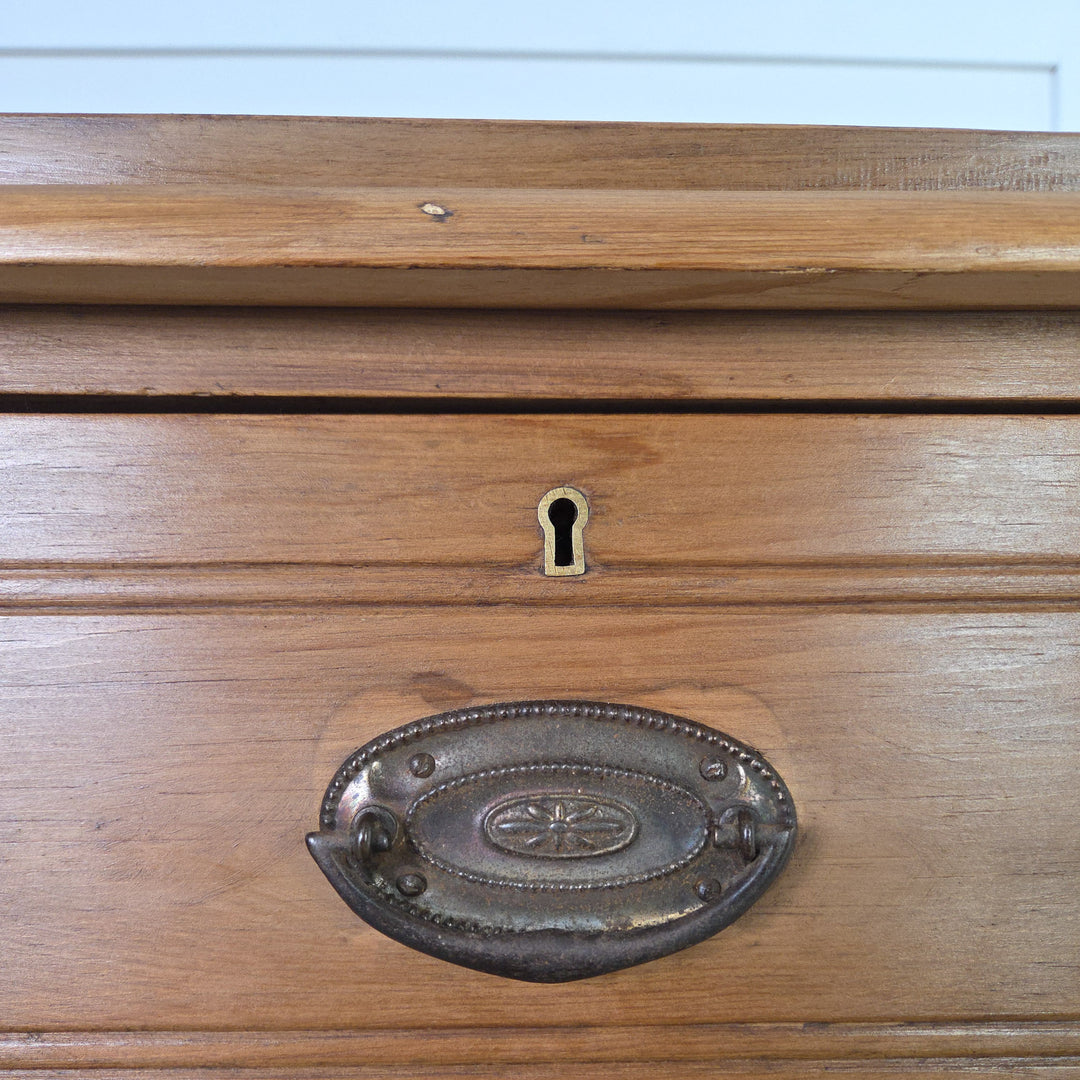 A rustic Edwardian satinwood chest of drawers offering four practical storage drawers with reeded detailing and brass swing handles, raised on tulip-shaped feet and finished in Briwax Rustic Pine to highlight the natural grain.