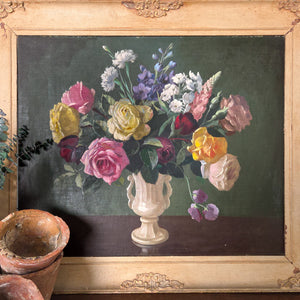A vintage 20th century still life floral oil painting on board showing radiant pink and yellow flowers arranged in a decorative vase. Signed to the lower left, the composition is framed in painted wood, giving definition to the subject and creating presence for display in the home.