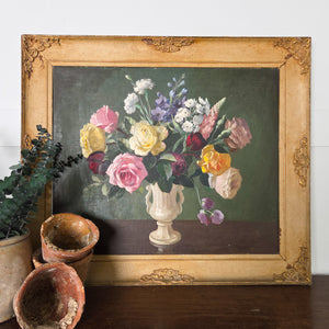 Vintage floral oil painting, mid 20th century, signed, showing a decorative vase of blushing pinks and golden yellow blooms set against a dark background. The work is presented in a painted frame, giving it a complementary finish and making it suitable for traditional interior styling.