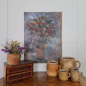 French oil painting from the early 20th century showing a potted plant with red and green leaves, painted with expressive brushwork and soft tonal contrast. The terracotta pot sits on a cool blue-grey surface with a gentle, aged appearance.