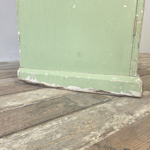An early 20th-century French painted cupboard in worn soft green, with two doors opening to eight internal drawers that graduate in depth and feature slatted bases. The shaped plinth and overhanging cornice add to its farmhouse country character, creating a practical antique storage cupboard with strong visual appeal.
