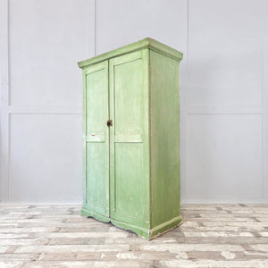 A rustic early 20th-century French painted cupboard in green, fitted with two doors and eight internal drawers with slatted bases. The shaped plinth and overhanging cornice add to its cottage and country style character, creating a well-proportioned antique storage cupboard with useful internal space.