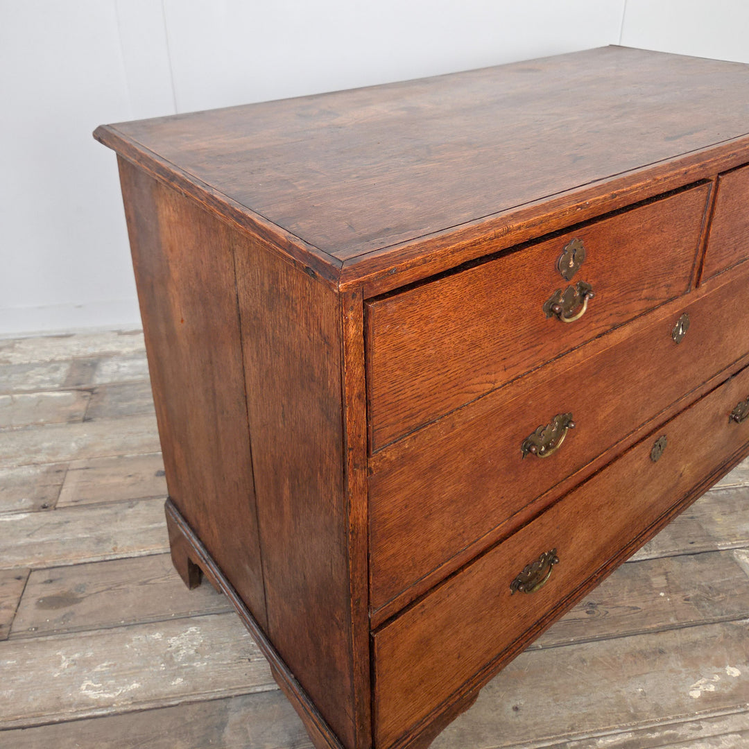 A classic Georgian oak chest of drawers from the early 19th century, with four drawers, brass handles and bracket feet. A useful antique storage piece with a rich oak tone.