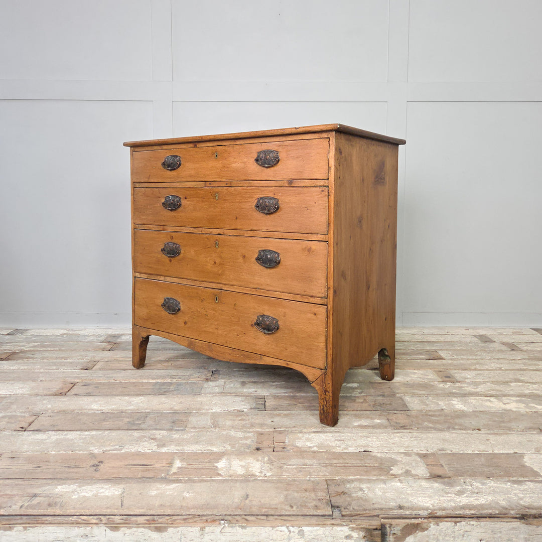 A 19th-century Georgian chest of drawers crafted from pine, with oval brass handles and a shaped apron. A timeless antique furniture piece for farmhouse-inspired spaces, perfect for use as bedroom storage or as a sideboard in a period home.
