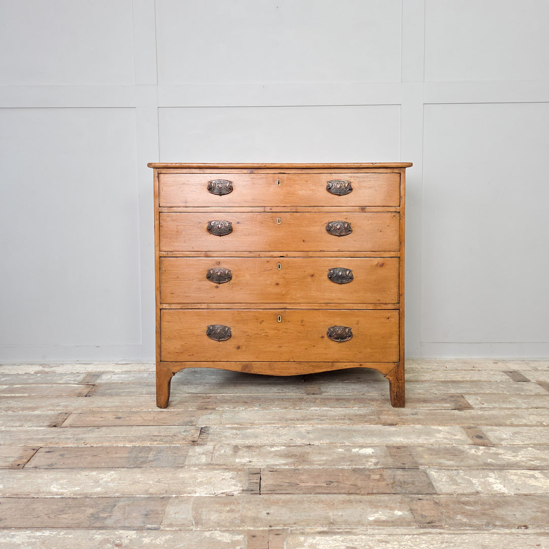 A Georgian pine chest of drawers from the early 1800s with five drawers, brass pulls and a shaped lower apron. A characterful piece of antique bedroom storage, ideal for traditional or rustic interiors, hallways or living rooms styled with antique pine furniture.