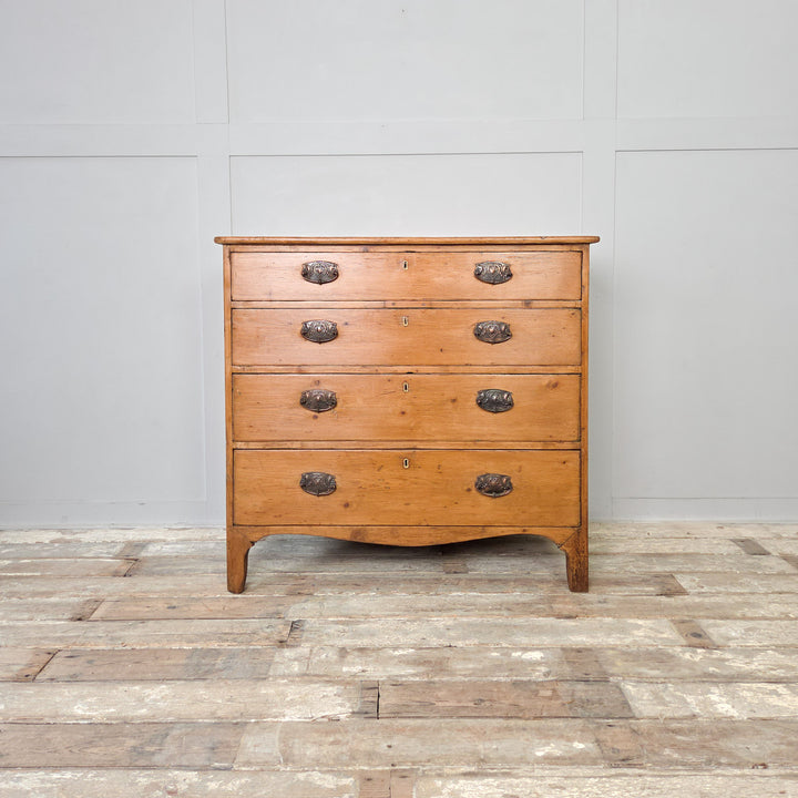 A Georgian pine chest of drawers from the early 1800s with five drawers, brass pulls and a shaped lower apron. A characterful piece of antique bedroom storage, ideal for traditional or rustic interiors, hallways or living rooms styled with antique pine furniture.