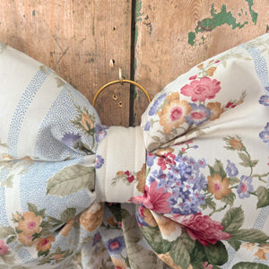 A handmade vintage floral stripe bow from Jennings & Cox, padded and structured with elongated tails for hanging. Finished with an antiqued brass ring, this Country House Bow offers versatile styling for doors, mantels, shelves, and decorative displays.